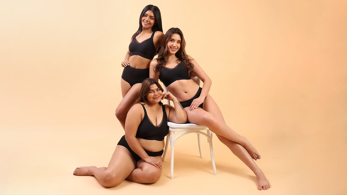 Three women wearing oh, so u bello black bra posing together against a beige background, showcasing inclusive sizing and body confidence